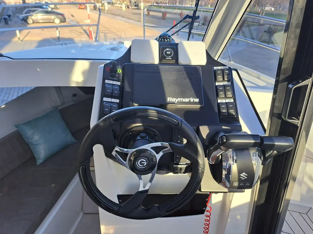 Boat cockpit interior featuring a steering wheel, Raymarine display, control buttons, and a plush seating area.
